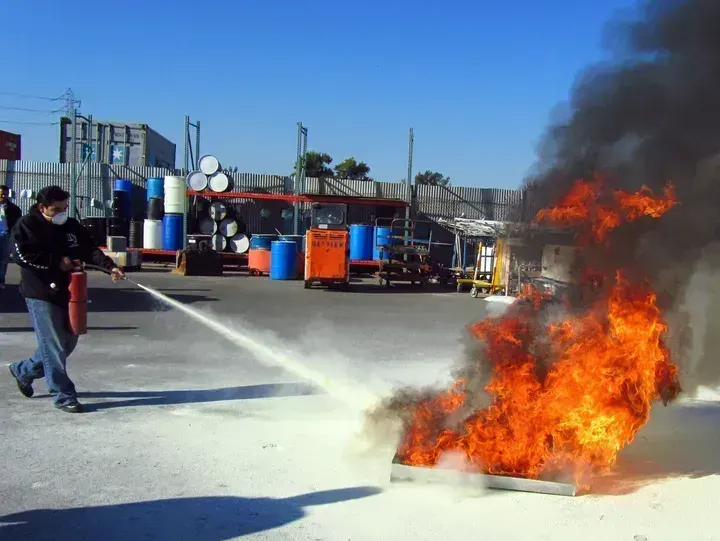 A person using a red fire extinguisher to put out a fire in a metal pan outdoors