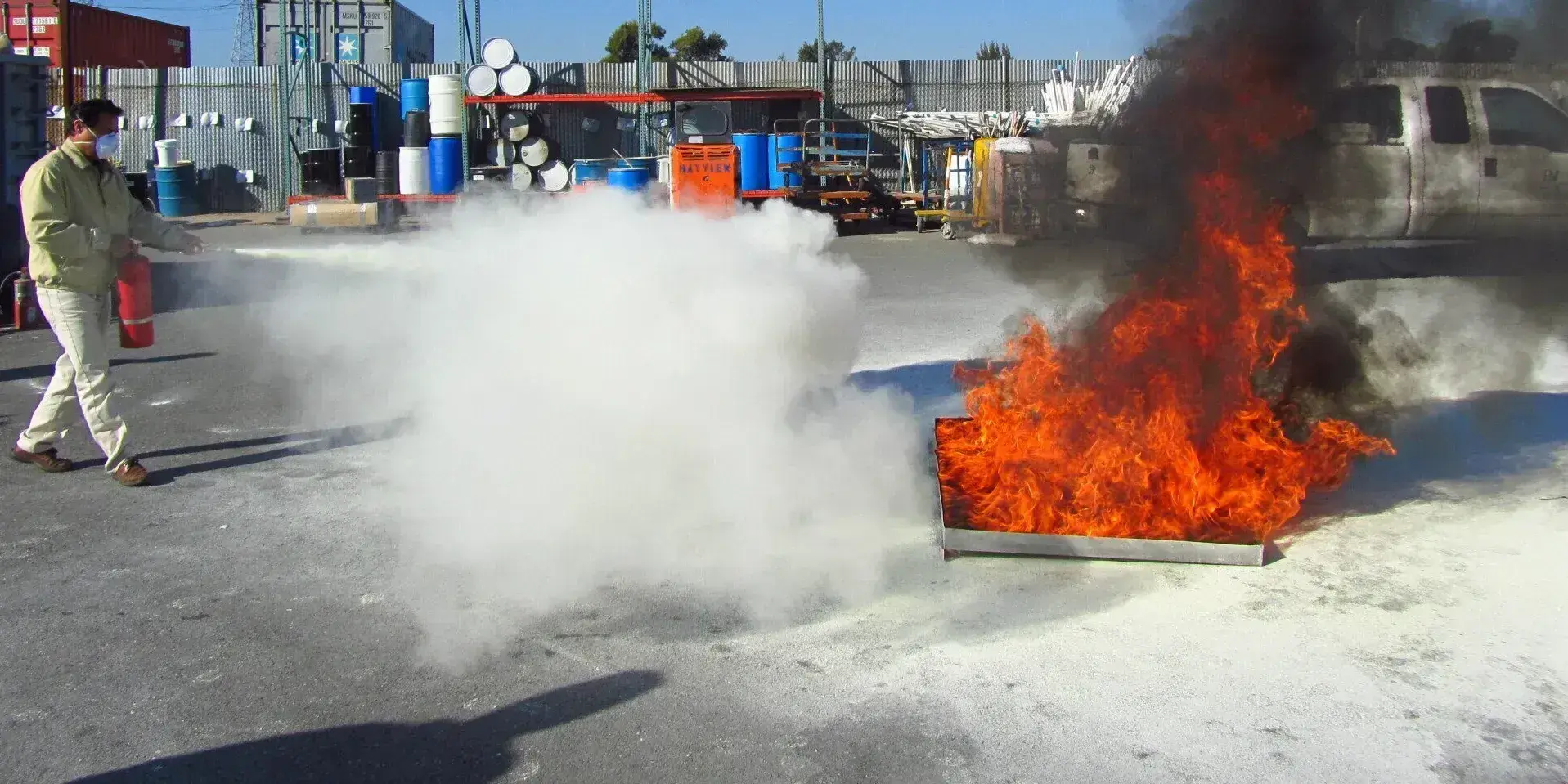 A technician sprays a fire extinguisher at a live pan fire during a hands-on fire extinguisher training demo